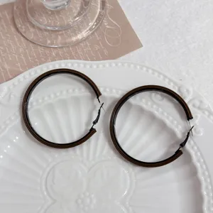 Detailed view of oversized brown and black geometric hoop earrings on a decorative plate