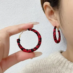 Close-up of red and black leopard print leather braided hoop earrings on ear and hand.
