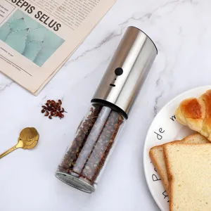 Detail view of a stainless steel electric pepper grinder on a marble table with bread.