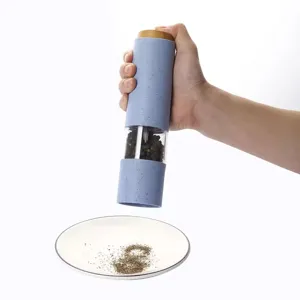 Action-Shot: Blaue Pfeffermühle aus Weizenstroh mahlt Gewürze auf einen weißen Teller