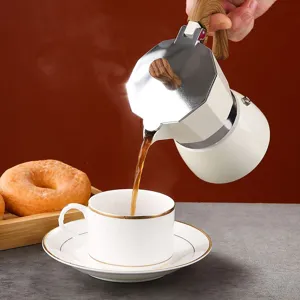 Professional white espresso Moka pot with wood grain handle pouring coffee into a ceramic cup
