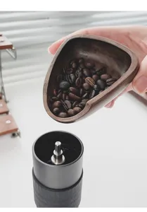 Primer plano de bandeja de madera para café vertiendo granos en un molinillo negro