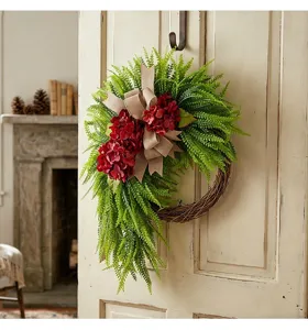 Red hydrangea and green fern wreath with a burlap bow hanging on a rustic white door