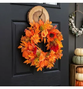 Close-up of harvest autumn wreath with orange maple leaves and sunflowers on black door