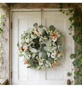 Rustic artificial lamb's ear wreath with white pumpkins and orange berries on a white door