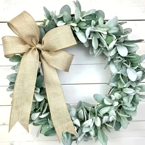 Close-up of a spring lamb's ear wreath with a large burlap bow on white wood slats.
