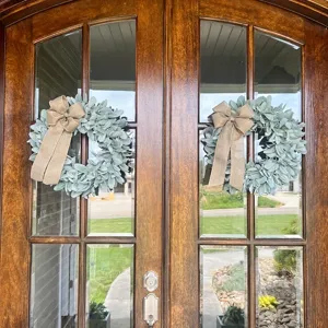 Pair of artificial lamb's ear wreaths with burlap bows on a wooden front door.