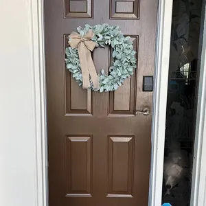 Artificial lamb's ear wreath with a burlap bow hanging on a rustic brown front door
