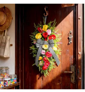 Festón de rosas artificiales con lazo de rayas colgado en una puerta de madera rústica
