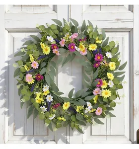 Vue détaillée d'une couronne de fleurs printanières avec marguerites sur une porte blanche