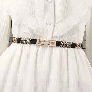 Close-up detail of a gold flower-shaped metal buckle and elastic band on a white dress