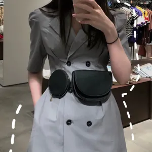 Elegante cinturón riñonera negro con bolsillos redondos y semicirculares sobre vestido gris.