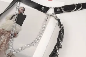 Dettaglio cintura punk goth in pelle con catena d'argento e accenti di anelli.