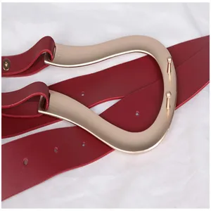 Gros plan d'une élégante ceinture rouge pour femme avec boucle en métal en U dorée