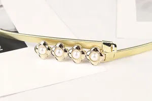 Macro view of a gold metallic elastic waist belt with four elegant pearl flower details
