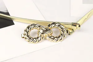 Close-up of elegant gold elastic metal chain belt featuring a textured interlocking buckle.