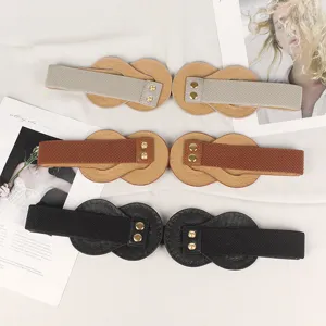 Close-up of three wide elastic waist belts in beige, brown, and black with metal rivet details