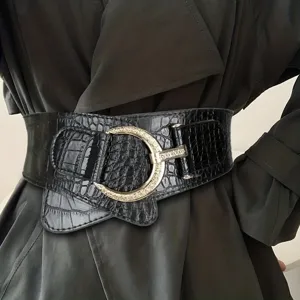 Close-up of wide black crocodile texture waist belt with large gold buckle on coat