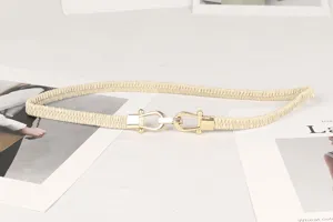 Detalle de un cinturón elástico crema con una hebilla de herradura en tono dorado.