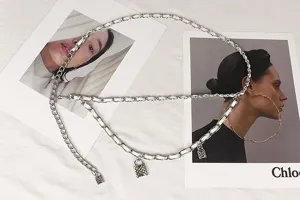 Close-up detail of silver woven metal chain waist belt featuring small padlock charms