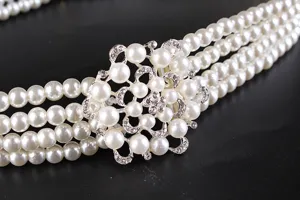 Close-up of elegant four-strand pearl belt with a sparkling rhinestone flower buckle