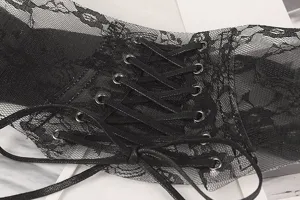 Close-up detail of black lace corset belt with metal eyelets and cross-tie ribbon