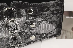 Macro detail showing black floral lace texture and silver metal rings on wide belt