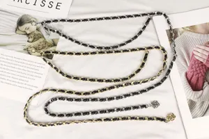 Detailed view of layered metal waist chain with camellia charm and leather weave.