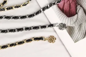 Macro detail of stylish metal chain belt featuring leather weaving and camellia charms.