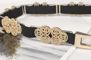 Close-up detail shot of a black elastic belt with golden intertwined metal buckle design