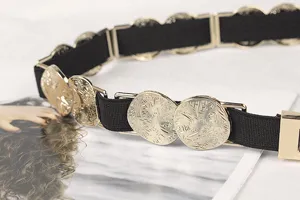 Close-up detail showing the textured gold metal plate on a thin black elastic belt.