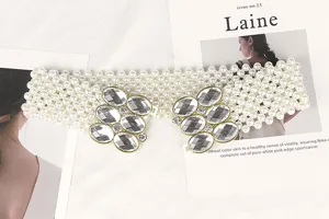 Detailed view of white elastic pearl belt with large floral rhinestone buckles.