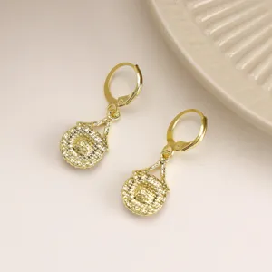 Close-up of elegant gold drop earrings featuring an intricate textured circular design.