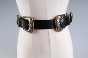 Dettaglio di cintura in pelle nera vintage con due fibbie dorate incise in stile retrò.