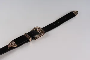 Dettaglio ravvicinato di una cintura nera vintage con fibbie in metallo dorato incise.