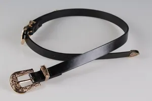 Dettaglio di cintura vintage nera Y2K con doppie fibbie dorate finemente incise.