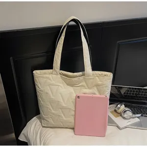 Bolso tote acolchado beige grande junto a una tableta rosa para referencia de tamaño