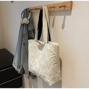Vista detallada de un bolso tote acolchado crema con patrón en V colgado en un perchero