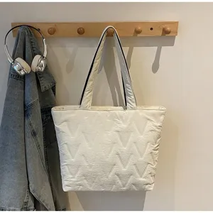 Detalle de bolso tote blanco de gran capacidad con relieve de patrón V en un perchero.