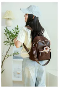 Stylish brown quilted women's backpack with cute pom-pom charm shown on model