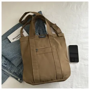 Close-up of brown canvas crossbody bag showing front zipper pocket and denim prop.