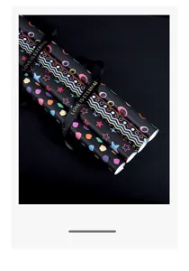 Détail de rouleaux de papier cadeau noir avec motifs colorés et ruban inscrit doré.