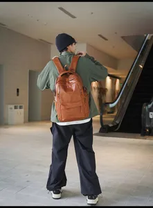 Vista trasera de un modelo con una gran mochila de cuero marrón vintage en un centro comercial.