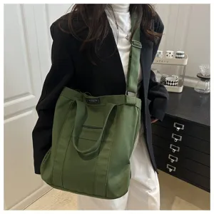 Large green canvas tote bag shown worn as a crossbody bag for a casual street style