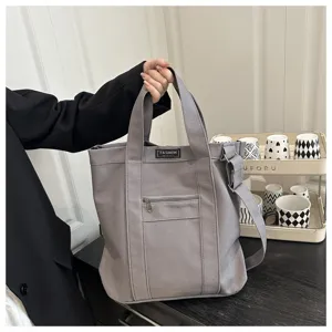 Minimalist gray canvas tote bag with front zipper pocket and adjustable shoulder strap.
