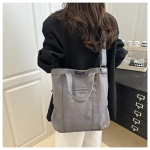 Detailed view of the gray canvas tote bag featuring front zipper pocket and straps.