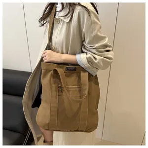 Stylish large brown canvas tote bag with shoulder strap worn by a female model outdoors
