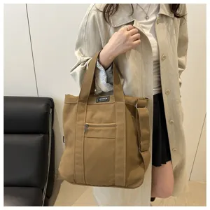 Lifestyle detail of a large khaki canvas tote bag worn by a model in a trench coat