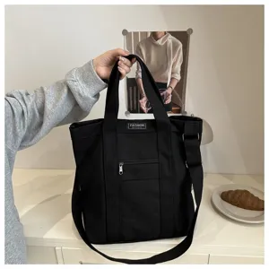 Hand-held view of a minimalist black canvas tote bag with adjustable shoulder strap
