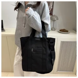Woman wearing a large black canvas crossbody tote bag in a casual indoor setting